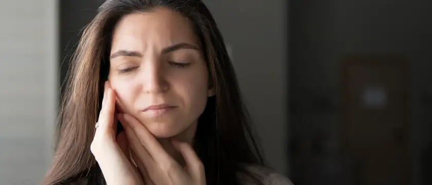 Mujer tocándose la mandíbula por dolor causado por bruxismo